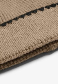 Knitted blanket in beige with a ribbed texture, featuring a black scalloped accent along the edge. Soft, warm fabric with a cozy appearance.