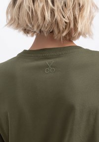 T-shirt verde oliva con collo rotondo e un sottile logo a forbice impressa sul retro, realizzata in morbido cotone.