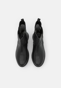 Botas de cuero negro hasta el tobillo con una textura suave, puntera circular y cremalleras laterales. Presentan tiradores para un calce fácil.
