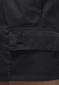 Pantaloni shorts neri con una texture opaca, dotati di un logo Jordan ricamato sulla tasca laterale e un design semplice e funzionale.