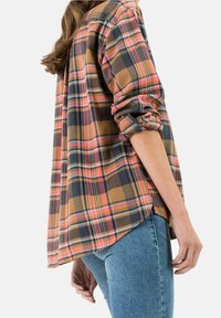 Camicia a quadri in tonalità terrose di marrone, arancione e blu navy. Caratterizzata da maniche arrotolate, orlo curvo e vestibilità ampia.