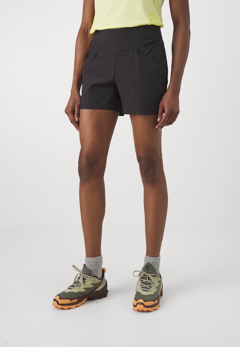 Pantalones cortos deportivos negros con una cintura alta, dos bolsillos frontales y una tela ligera y transpirable, combinados con zapatillas de senderismo multicolores.