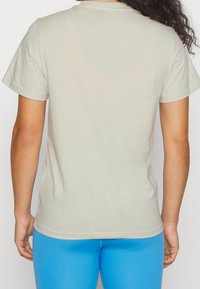 Lys beige kortærmet t-shirt med klassisk rund hals og glat bomuldsstof; bagvæggen viser en afslappet pasform og minimalistisk design.