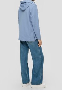 Sudadera azul claro de tela suave con capucha, combinada con unos pantalones vaqueros de denim azul de corte holgado y zapatillas de plataforma blancas.