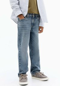 Ljusblå jeans med avslappnad passform, en klassisk femficksdesign och subtila blekta accenter, i kombination med grå tygskor.