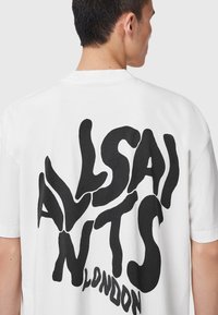 Camiseta de algodón blanca con gran texto abstracto negro que dice "ALLSAINTS LONDON" en la parte de atrás. Mangas cortas y escote redondo.
