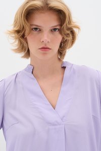 Blusa lavanda con scollo a V e dettaglio arricciato al colletto. Realizzata in tessuto liscio, presenta maniche corte e un design minimalista.