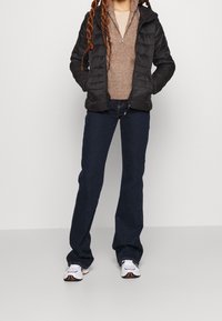 Svart puffjacka, brun stickad halvdraget tröja, mörkblå utsvängda jeans och vita sneakers med färgglada detaljer. Avslappnad lagerlook.