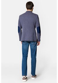 Granatową marynarkę w kratę z kontrastującymi niebieskimi łatami na łokciach, dopasowany krój, w zestawieniu z niebieskimi dżinsami i szarymi sneakersami widzianymi z tyłu.