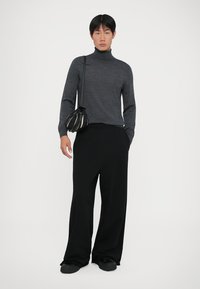 Grå polotröja, vida svarta byxor och en liten, strukturerad svartvitt väska. Minimalistisk design med avslappnad passform.