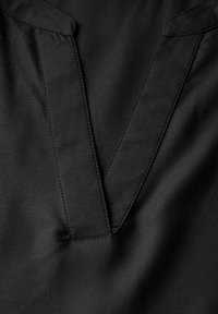 Camicia in tessuto nero con scollatura a V. La texture è liscia, con raffinati cuciture lungo il collo e la patta.