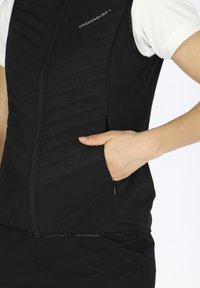 Schwarzes ärmelloses Vest mit gestepptem Textur, Frontreißverschluss, Seitentasche und SWEDEMOUNT-Branding am Saum. Glattes Material.
