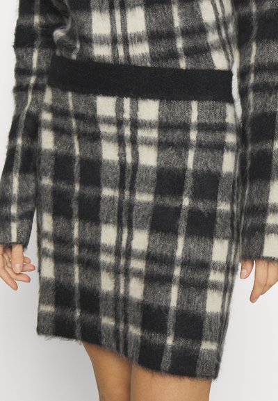 Pletena karo krila s črno, sivo in krem barvno paleto, mehko teksturo in širokim pasom. Robovi so rahlo razfrkani.