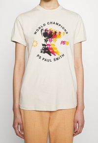 Camiseta de algodón color crema con un gráfico colorido de un trofeo y manos, con el texto "CAMPEONES DEL MUNDO" y "PS PAUL SMITH." Mangas cortas.