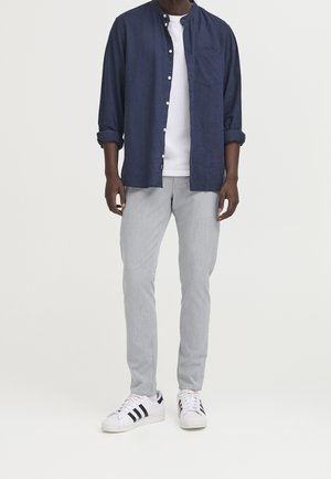 Granatowa koszula na guziki, biała koszulka pod spodem, szare spodnie oraz białe trampki z czarnymi paskami. Codzienny strój z podwiniętymi rękawami koszuli.