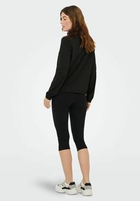 Maglia nera a maniche lunghe con scollo rotondo, abbinata a leggings neri corti e sneakers bianche chunky con dettagli neri; texture liscia.