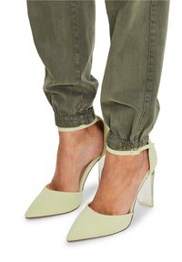 Jasnozielone szpilki z wąskim noskiem, przezroczystym blokowym obcasem i paskiem wokół kostki. Połączone z oliwkowo-zielonymi spodniami typu tapered.