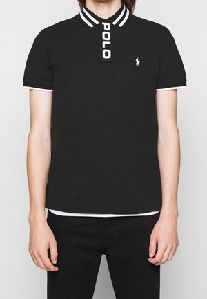 Personne portant un polo noir avec col et manches rayés blancs, texte « POLO » sur la patte de boutonnage et logo cheval blanc sur la poitrine gauche.