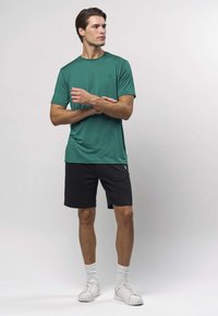 Groen sportief T-shirt met korte mouwen en ronde hals, gecombineerd met zwarte short, stof lijkt glad, model draagt witte sneakers.