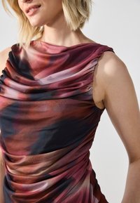 Robe au design drapé dans des couleurs dégradées riches de bordeaux, crème et bleu foncé, avec un tissu doux et texturé et des détails froncés.