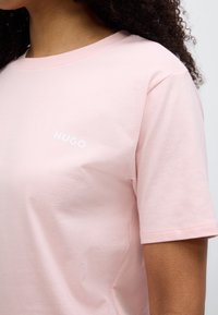 Κοντομάνικο ροζ βαμβακερό μπλουζάκι με στρογγυλή λαιμόκοψη και λευκό λογότυπο «HUGO» στο αριστερό στήθος. Ομαλή υφή, χαλαρή εφαρμογή.