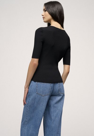 Schwarzes Rippstrick-Oberteil mit kurzen Ärmeln, das über einen dezenten V-Ausschnitt und eine figurnahe Silhouette verfügt. Kombiniert mit hellblauen, hoch taillierten Jeans.