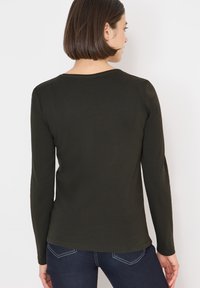 Camicia a maniche lunghe di colore verde scuro, realizzata in materiale morbido. Presenta una scollatura rotonda e una silhouette aderente. La vista posteriore mostra un orlo leggermente curvo.