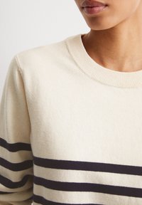Maglione beige con scollatura tonda, caratterizzato da strisce orizzontali blu navy. Texture morbida, colletto a costine e vestibilità strutturata.