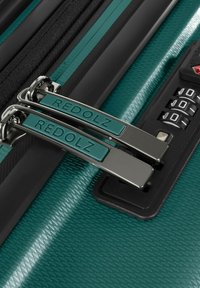 Primo piano di tirazip della valigia teal etichettati "REDOLZ" bloccati in un lucchetto a combinazione nero.