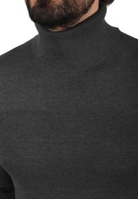 Suéter de cuello alto gris oscuro hecho de tela de punto, con una textura suave, cuello acanalado y un patrón sutil en el pecho.