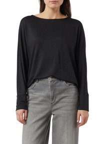 Czarna koszula z długim rękawem o luźnym kroju i szerokim dekolcie, wykonana z błyszczącego, teksturowanego materiału, zestawiona z jasnoszarymi jeansami o szerokich nogawkach.