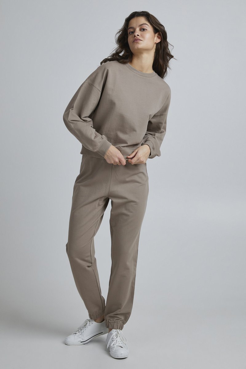 Felpa beige in cotone con maniche lunghe e vestibilità rilassata, abbinata a pantaloni tapered coordinati. Indossata con sneakers bianche.