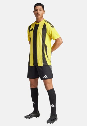 Yellow and black striped soccer jersey, black shorts, black socks, and cleats. Features Adidas branding and dynamic design lines.