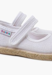 Hvid tekstil sko med to justerbare Velcro stropper, runde udskæringer og en vævet jute sål. Har et farverigt "pisamonas" mærke.