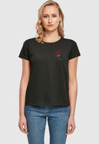 Sort bomulds t-shirt med et lille rødt hjerte-design på venstre bryst, korte ærmer og en afslappet pasform.