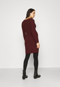 Bordeaux ribbeljurk met lange mouwen, aansluitende silhouette en ronde halslijn, gecombineerd met zwarte panty's en enkellaarsjes.