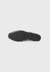 Semelle en caoutchouc noir avec une adhérence texturée ; la tige présente un design tissé en motifs beige et noir, créant une surface texturée.
