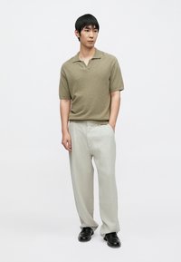 Πράσινο χακί πλεκτό πόλο μπλουζάκι με κοντό γιακά, συνδυασμένο με ανοιχτό γκρι φαρδιά παντελόνια και μαύρα μοκασίνια.