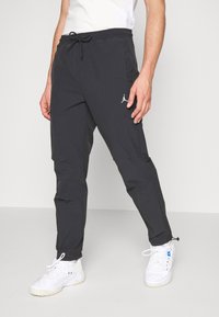 Zwarte lichtgewicht joggerbroeken met een trekkoord in de taille, zijzakken en een wit Jordan-logo op de linker dij. Glad stofoppervlak.