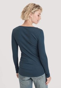 Langsleeve shirt in donkergroen, met een wijde halslijn en een getailleerde silhoeët. Materiaal lijkt zacht met een gladde textuur. Achteraanzicht weergegeven.