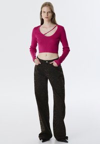 Un pull court en rib d'une couleur fuchsia avec un col large et des manches longues, associé à un pantalon large à imprimé léopard marron foncé.