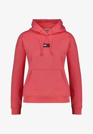 Hoodie rose corail avec une grande poche avant, capuche à cordon, et un petit logo noir et blanc sur la poitrine. Présente des poignets et un ourlet côtelés.
