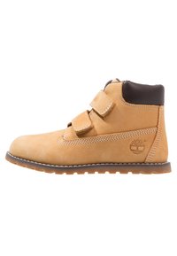 Botín de ante marrón con acentos de cuero marrón. Presenta dos correas de Velcro, costuras cosidas y una suela de goma texturizada. Logo de Timberland presente.