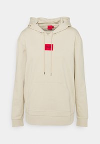 Felpa beige con cappuccio, caratterizzata da una patch rettangolare rossa con il logo "HUGO", cordini, tasca frontale a marsupio e polsini e orlo a coste.