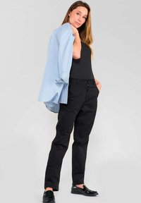 Zwarte broek gecombineerd met een strakke zwarte top en een lichtblauwe gestreepte oversized blouse. De blouse heeft opgerolde mouwen en een relaxte pasvorm.