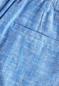 Tissu chevron bleu et blanc montrant un gros plan d'un vêtement sur mesure avec une poche cousue et un détail à la taille.