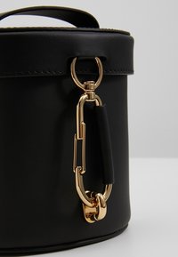 Rote Leder-Umhängetasche mit goldfarbener Schnalle und Beschlägen, glatter Textur und einem kurzen Griff mit einem kontrastierenden schwarzen Akzent.