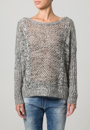 Suéter ligero y abierto en gris y negro con un escote amplio, mangas largas y puños acanalados. Combinado con jeans de mezclilla ajustados.