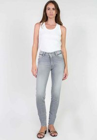 Jean skinny gris taille haute, légèrement délavé, à cinq poches, avec un bouton argenté. Associé à un débardeur blanc ajusté.