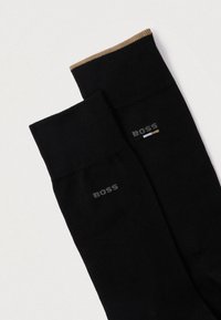 Μαύρες βαμβακερές κάλτσες με καφέ λεπτομέρεια στην κορυφή. Διαθέτουν το λογότυπο "BOSS" σε γκρι και μια μικρή πολύχρωμη ρίγα. Λείο υφή.